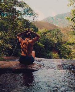 foto de uma mulher sentada de costas na pedra de uma cachoeira