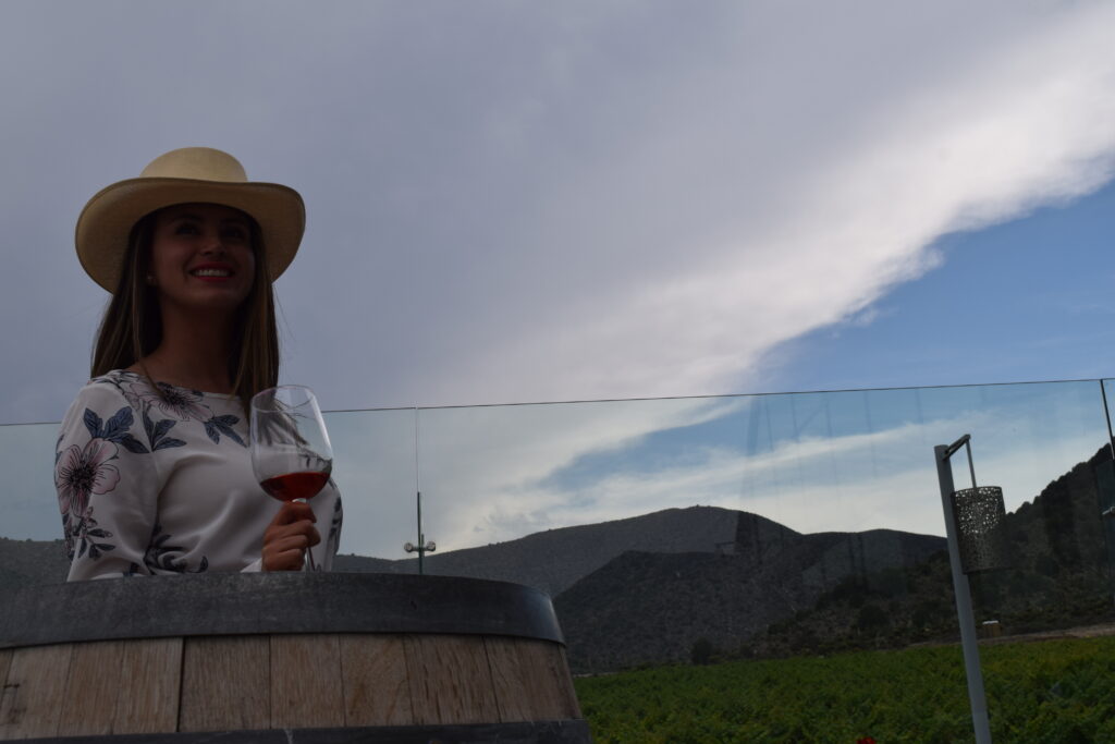 mujer con sombrero rojo y abanico rojo en terraza con montañas detrás 