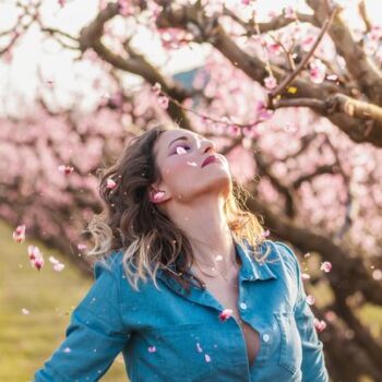 foto de uma mulher loira olhando para cima perto de uma árvore cm flores