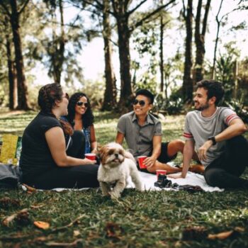 a group of friends sitting in the park with a white dog