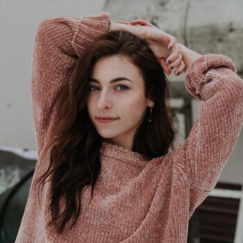 mujer con los brazos arriba y un suéter rosa