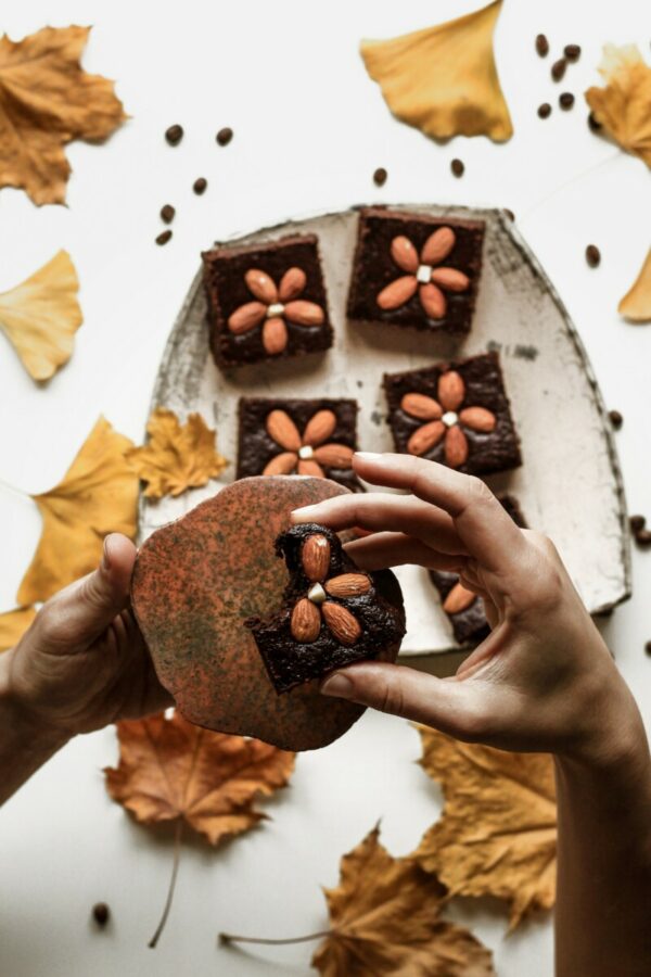 Foto de uma pessoa comendo brownie e uma forma com pedaços de brownies ao fundo