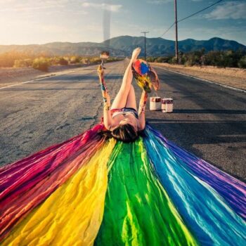 persona acostada en una carretera con una bandera de arcoíris