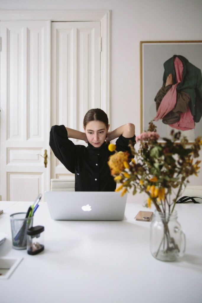 Foto de uma mulher sentada olhando para o computador com a mão na nuca