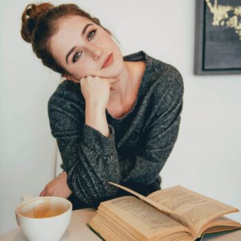 Woman with an open book and a cup of coffee looking to the camera