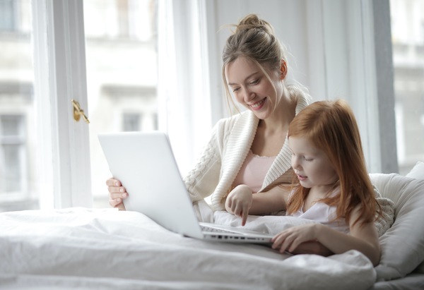 Mamá con su hija en la cama jugando con una computadora
