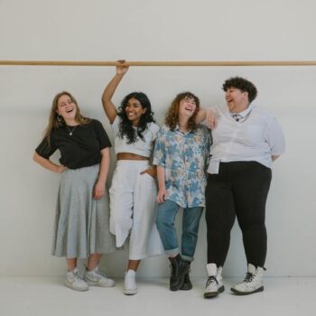 four women standing in front of a white wall laughing