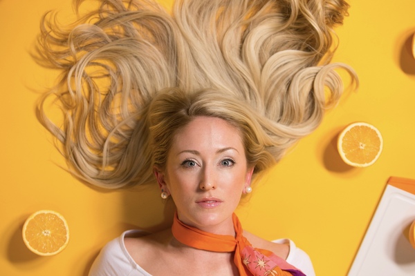 mujer acostada en un fondo amarillo con naranjas cortadas al rededor de ella