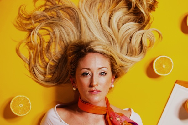 mujer acostada en un fondo amarillo con naranjas cortadas al rededor de ella