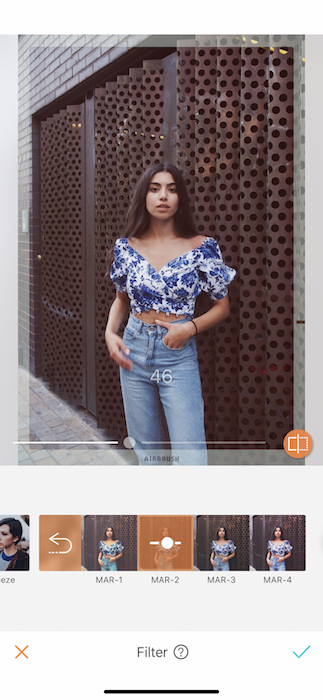  Kim Kardashian lookalike in blue jeans and floral top standing in front of metal wall