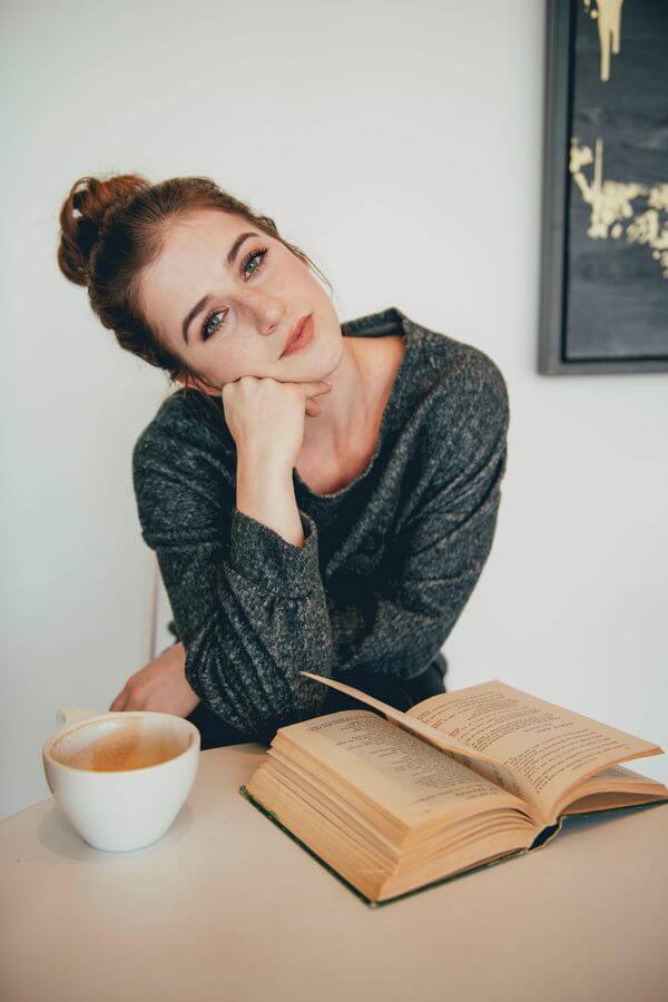 Mujer con un libro abierto sobre la mesa y una taza de café.