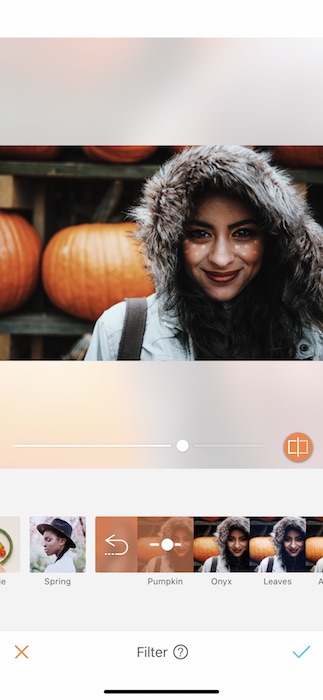 smiling woman wearing hooded jacket stands in front of pumpkins