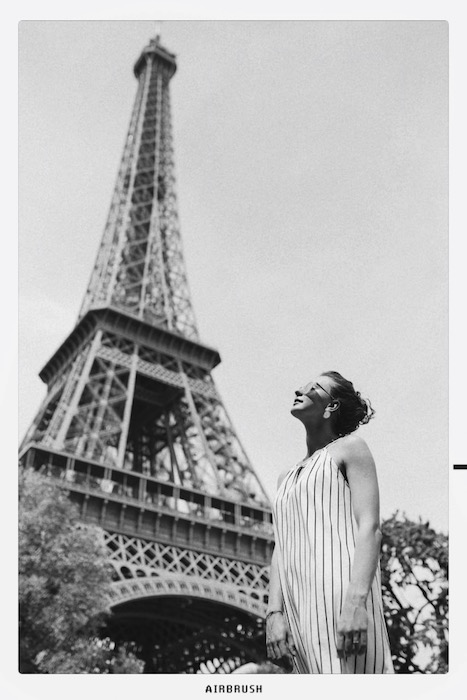black and white photo of white woman standing in front of the Eiffel Tower
