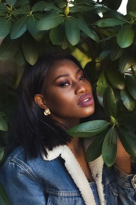black woman in denim jacket surrounded by green leaves