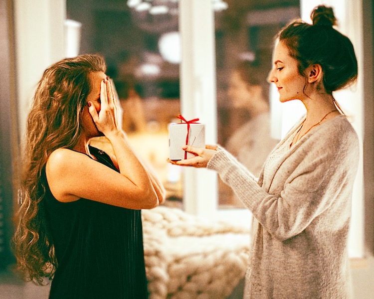 woman covers her eyes while another woman surprises her with a gift
