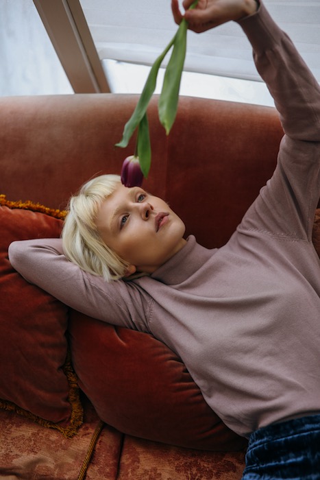 woman wearing a pink sweater lying on a sofa holding a flower