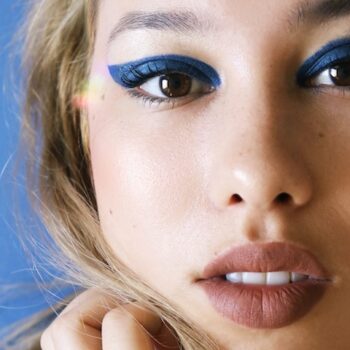 closeup of woman with blonde hair and blue eyeliner in front black background