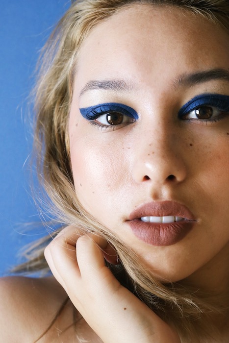 closeup of woman with blonde hair and blue eyeliner in front black background