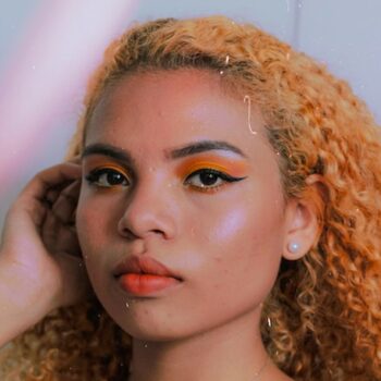 mujer con cabello afro naranja y maquillaje de ojos y labios naranja