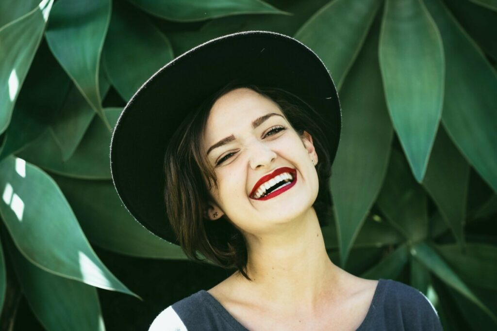 laughing woman wearing a hat in front of a leafy background