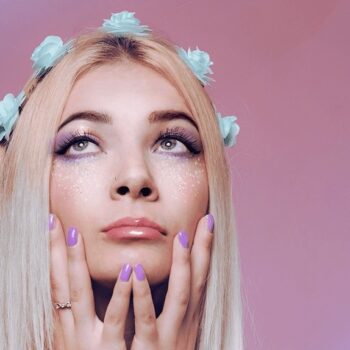 Pride Month edit of blonde woman with blue flowers in her hair in front of a pink background