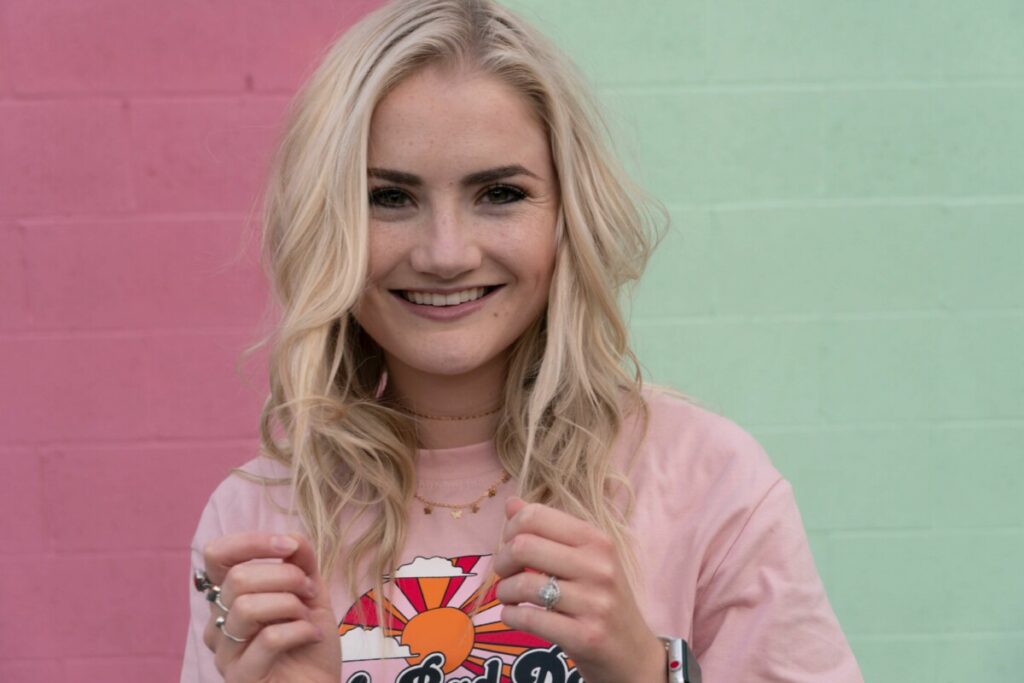 woman with blonde hair standing in front of a pink and green wall