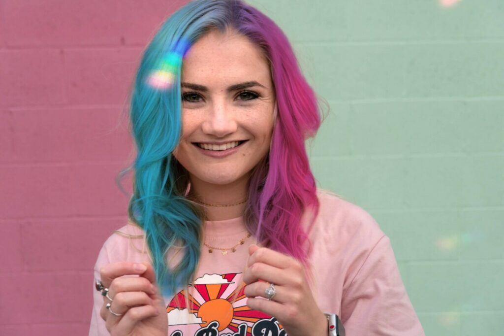 Pride Month edit of woman with blue and pink hair standing in front of a pink and green wall
