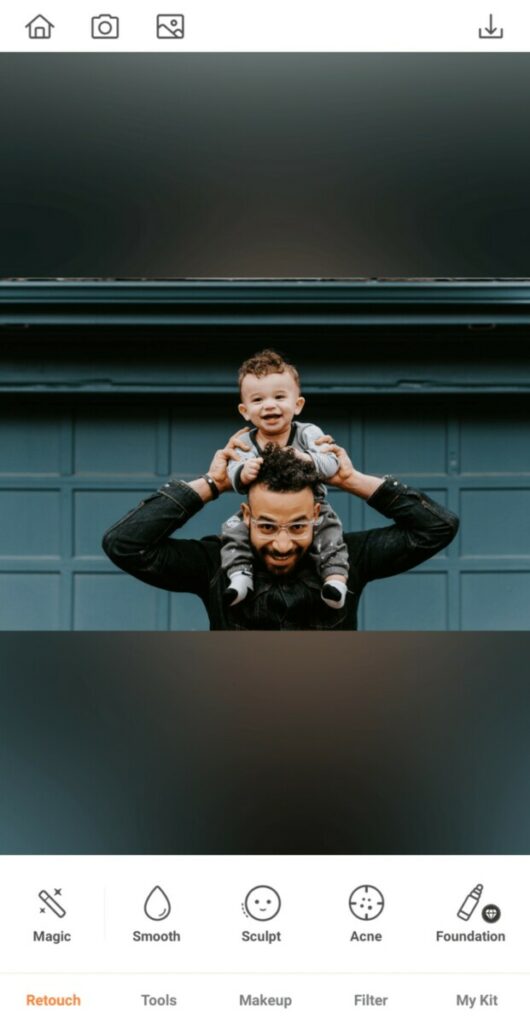 father holding his toddler son on his shoulders in front of green garage wall