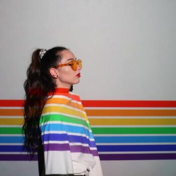 Garota em pé com as cores da bandeira LGBTQIA+ refletidas em sua jaqueta branca