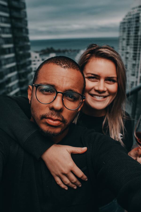 Homem de camisa preta com uma mulher abraçando-o