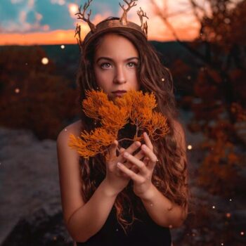 Garota com uma coroa de chifres de cervo segurando um ramo de folhas amarelas