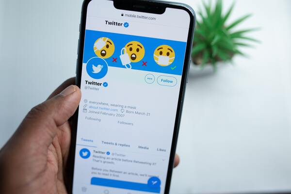Uma mão segurando um smartphone mostrando a tela inicial do Twitter
