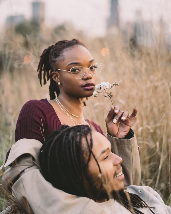 Garota negra segurando uma flor abraçada a um homem negro em um campo
