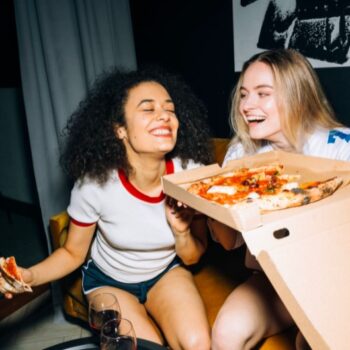 dos mujeres jóvenes comiendo pizza