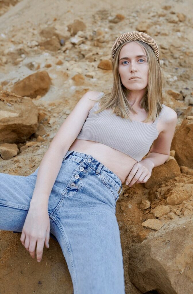 blonde woman wearing jeans and crop top sitting on rocks