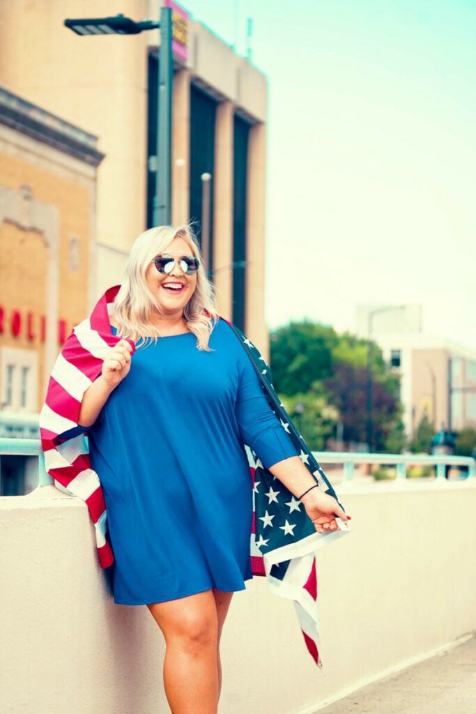 woman in blue dress and American flag celebrates July 4th