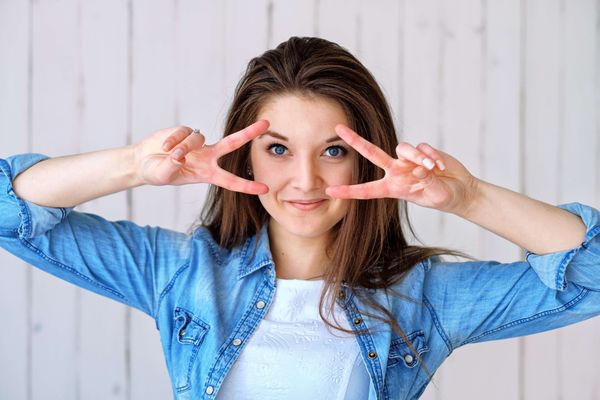 woman wearing chambray shirt making the peace sign over her eyes