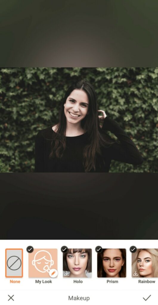 woman with dark hair and black sweater standing in front of greenery