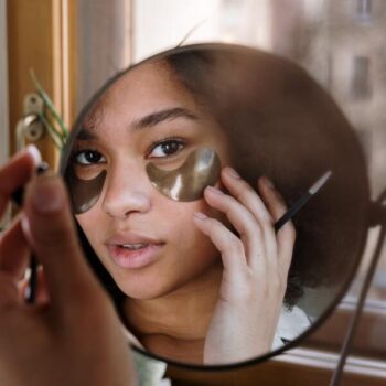 Foto tirada de um espelho com o reflexo do rosto de uma mulher negra fazendo skin care