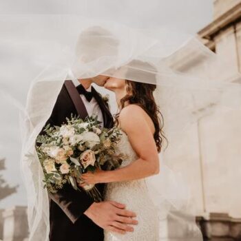 Casal durante o casamento deles se beijando debaixo do véu.