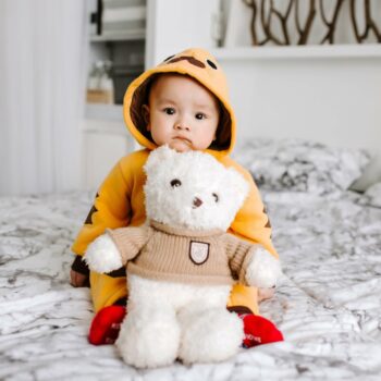 Baby on a bed with a teddy bear wearing chicken costume