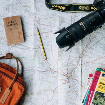 travel flat lay featuring a camera, backpack, notepad and map