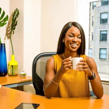 woman seated behind a desk holding a cup of coffee