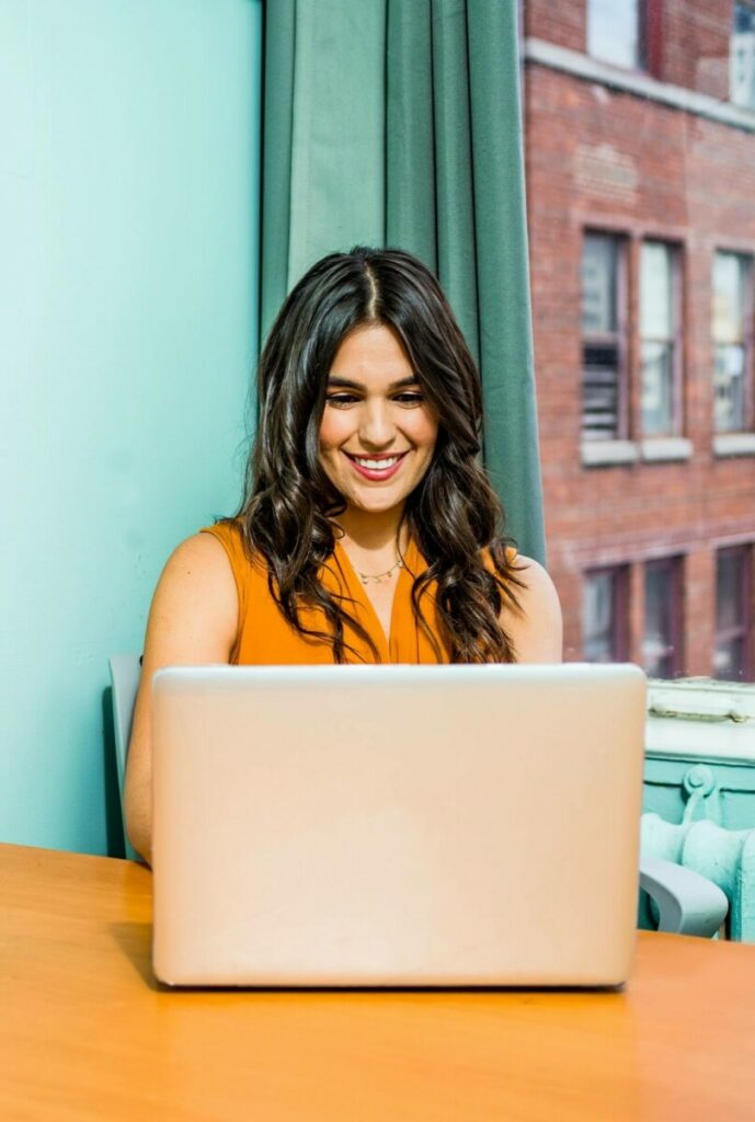 smiling woman in an office with blue walls typing on a laptop