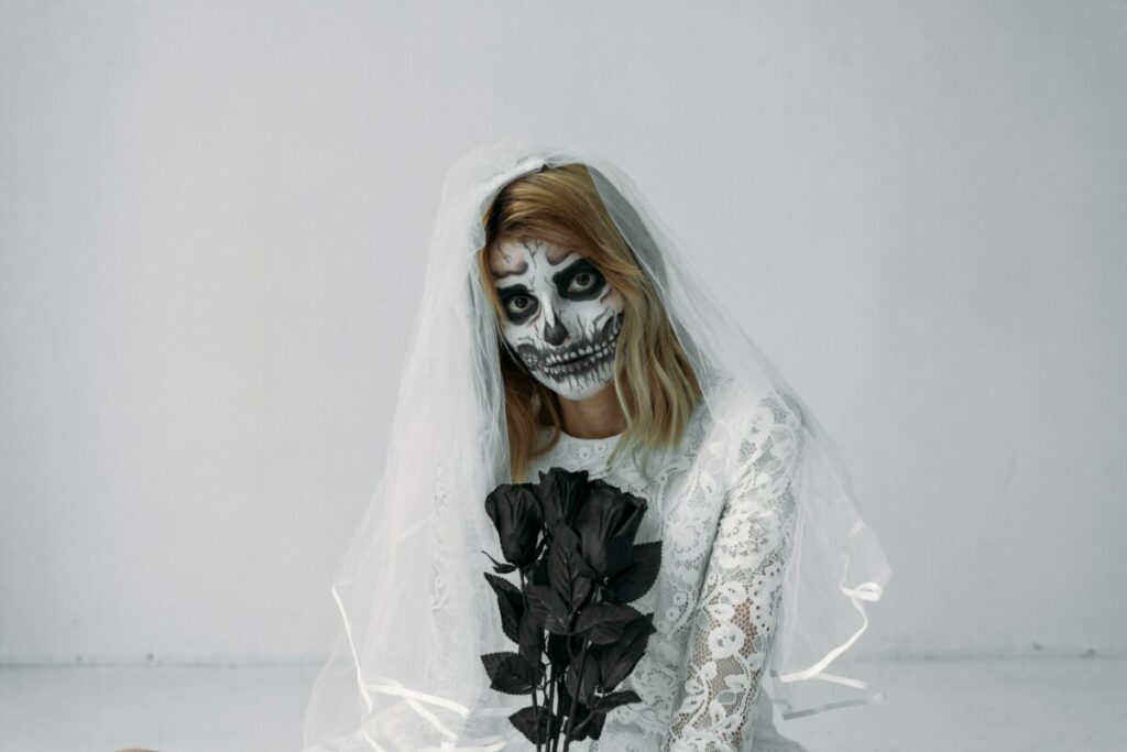 woman wearing skull makeup and a white dress poses with black roses