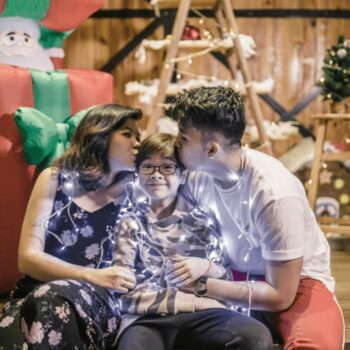parents kissing child wrapped in lights
