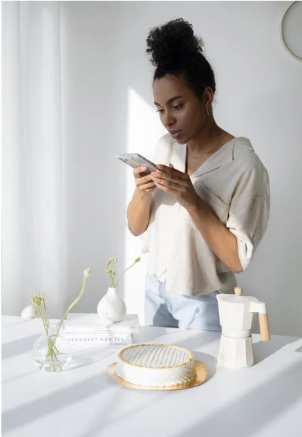 woman in a white shirt and jeans using her cell phone to take a photo of objects on a table